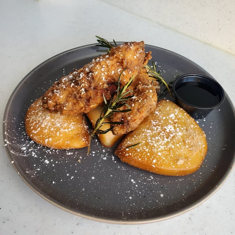 Fried chicken tenders and golden bao buns dusted with powdered sugar and rosemary, with a side of syrup.