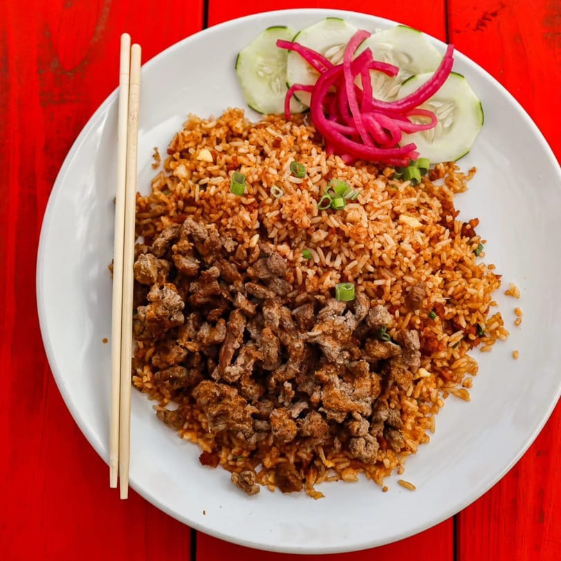 Asian fried rice with ground meat, green onions, pickled red onions, and cucumber slices.