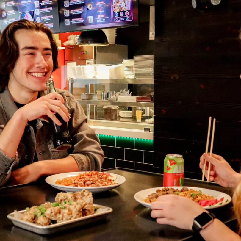 Two people enjoying Asian food and drinks at Chubby Bao House, with a smiling man holding a soda.