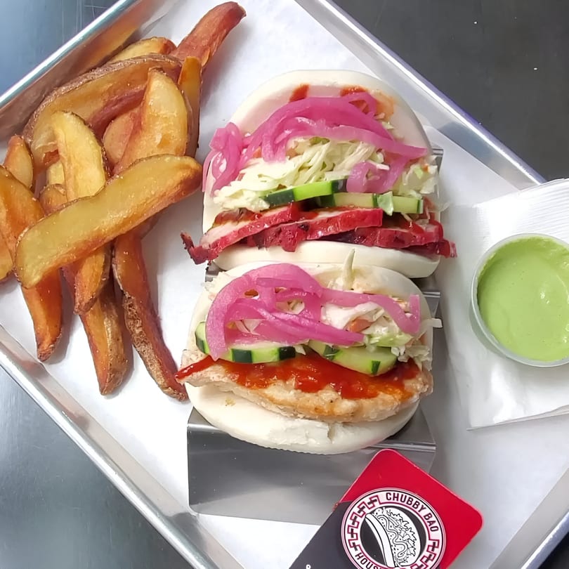 Two Chubby Bao House bao buns with fries and green sauce on a metal tray.