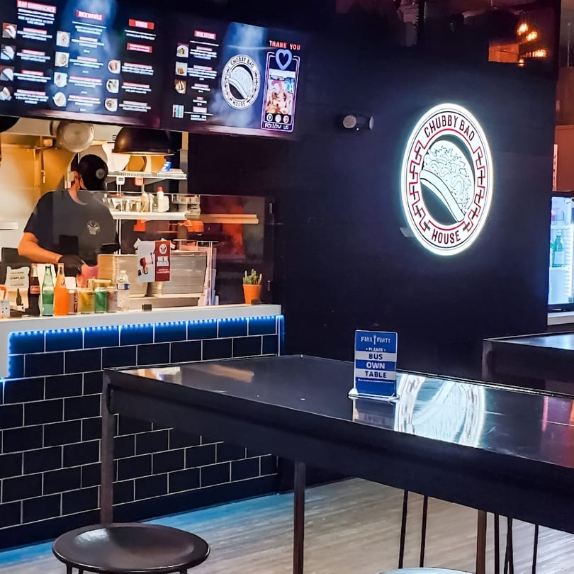 Chubby Bao House interior with a chef behind the counter, menu boards, and a neon logo.