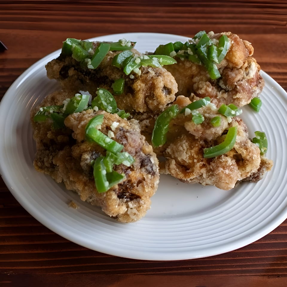 Crispy fried chicken pieces topped with chopped green peppers and garlic on a white plate.