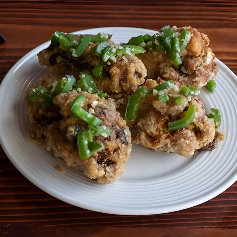 Crispy fried chicken pieces topped with chopped green peppers and garlic on a white plate.